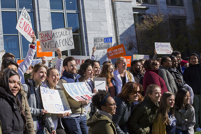 Dozens of students stand in front of the Emory School of Medicine with protest signs