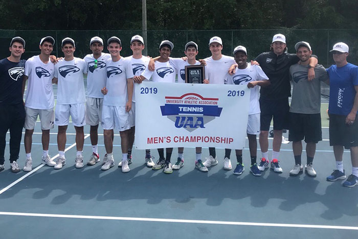 The Emory men's tennis team poses with a banner naming them UAA champions