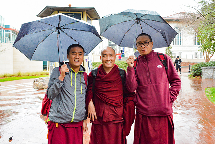 Three Emory students, including Tibetan monks, share a couple of umbrellas as they walk through Asbury Circle