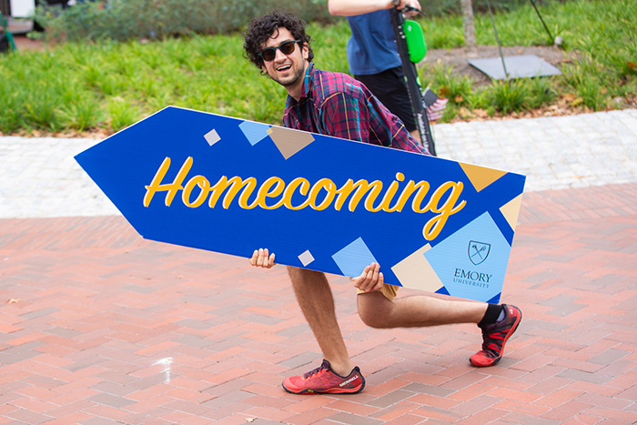 A student holds a sign that says "Homecoming" pointing others to his right