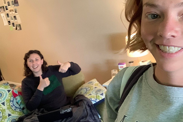 Georgia Brunner gives a thumbs-up from the couch while her roommate takes a selfie of the two of them