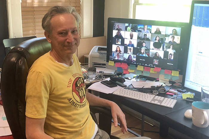 Clifton Crais poses in front of his computer while his class appears in boxes on a Zoom video call