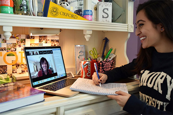 A student smiles at another student who is speaking to her over a web camera