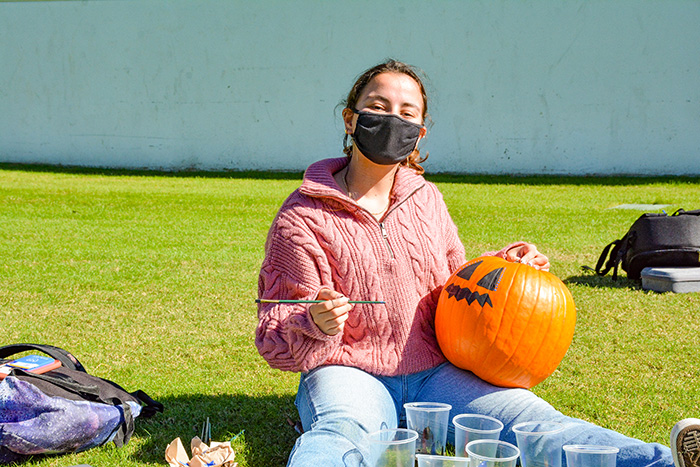 A young woman wearing a mask paints a pumpkin on the quadrangle