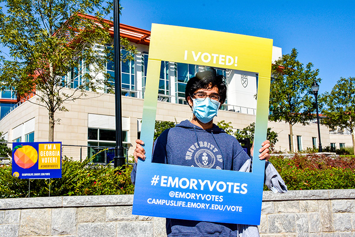 A student holds up a sign around his face that says "#EmoryVotes"