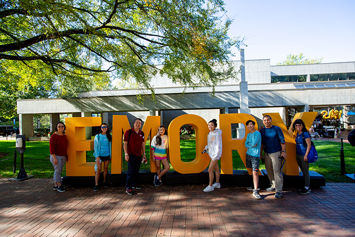 Students pose in front of a yellow Emory sign