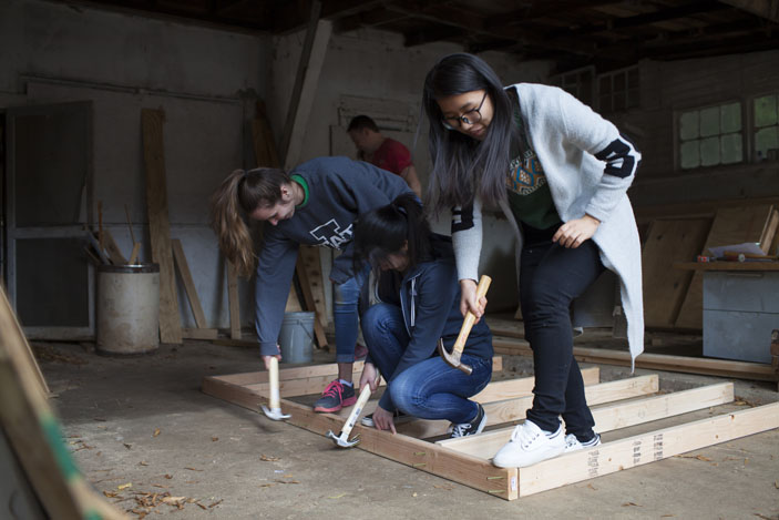 Three women volunteers with hammers nail together a wall section.