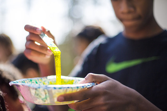 A teen boy stirs yellow-looking slime with a stick