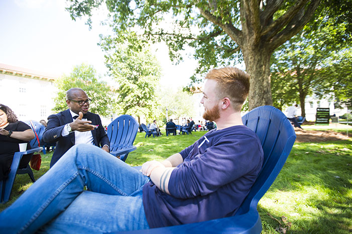 Two Emory community members speak with each other while seated in Adirondack chairs on the quadrangle