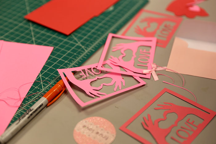 Detail of pink and red Valentine's Day cards showing the word "love" with hands making a heart symbol. 