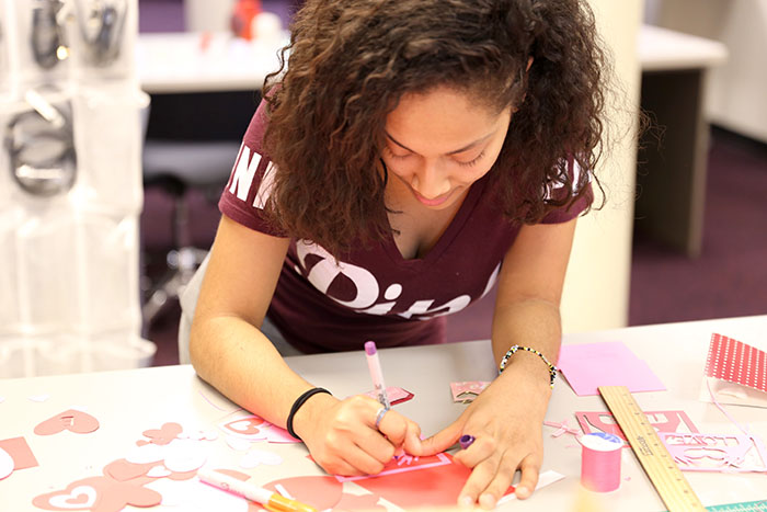 A female student works at a craft table to cut out paper hearts.