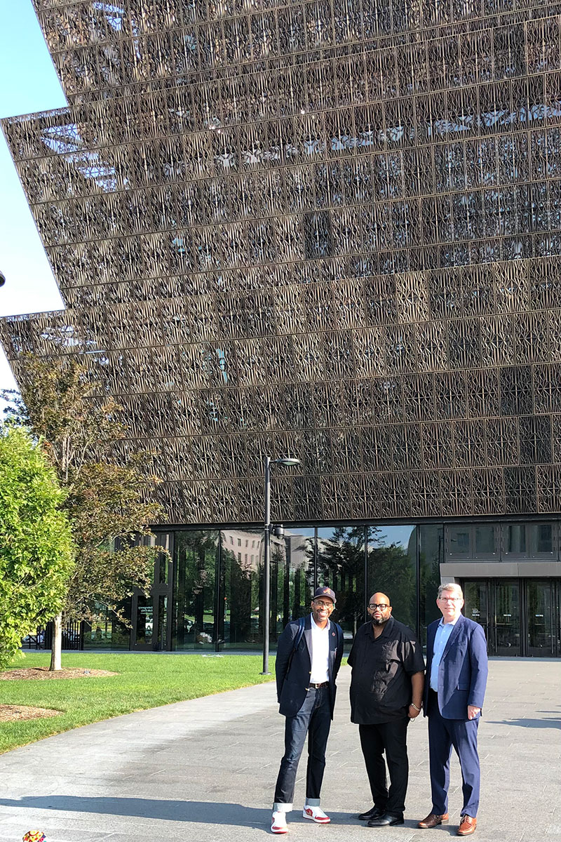 Three men stand in front of the National Museum of African American History and Culture in Washington, D.C.