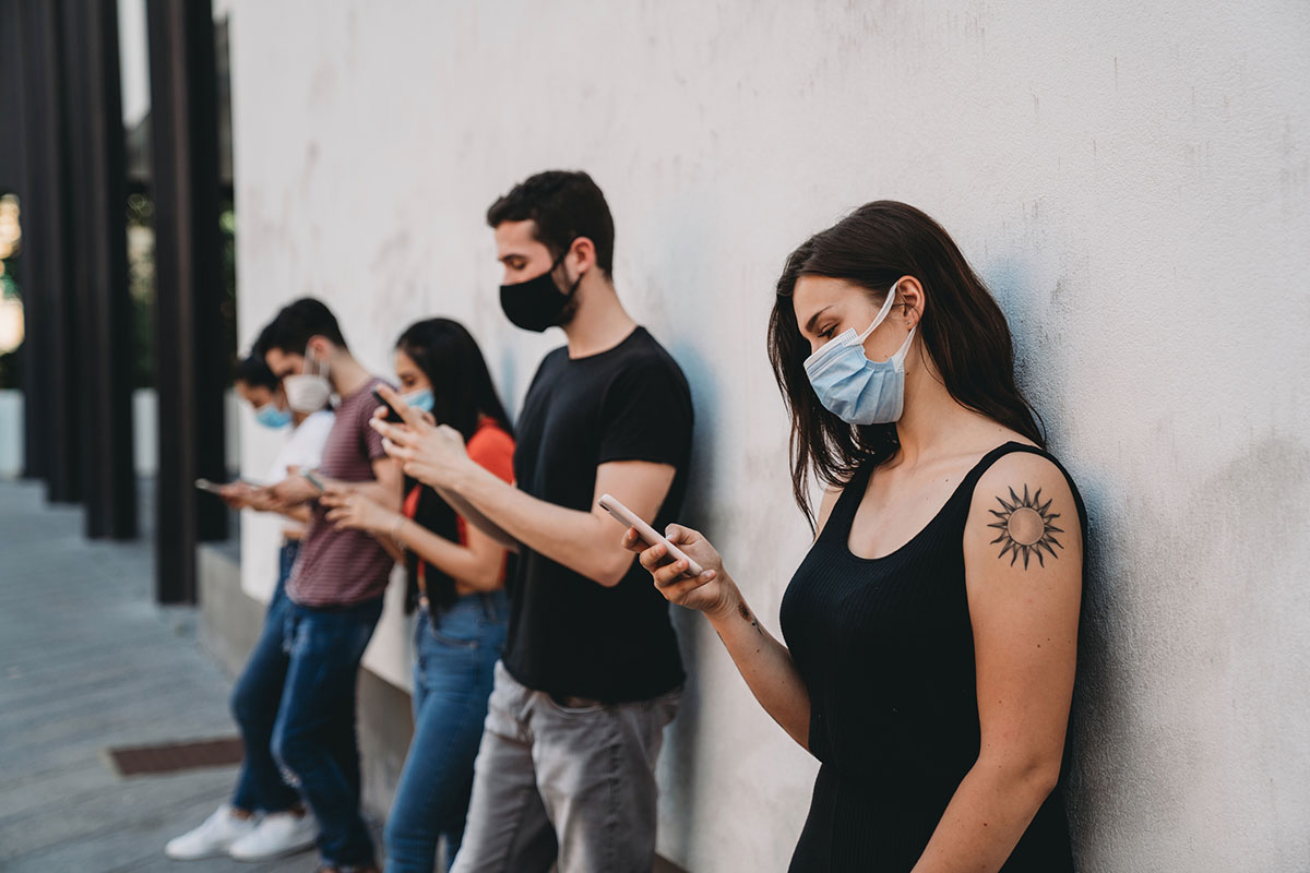 A group of individuals wearing different kinds of masks while looking at their phones.