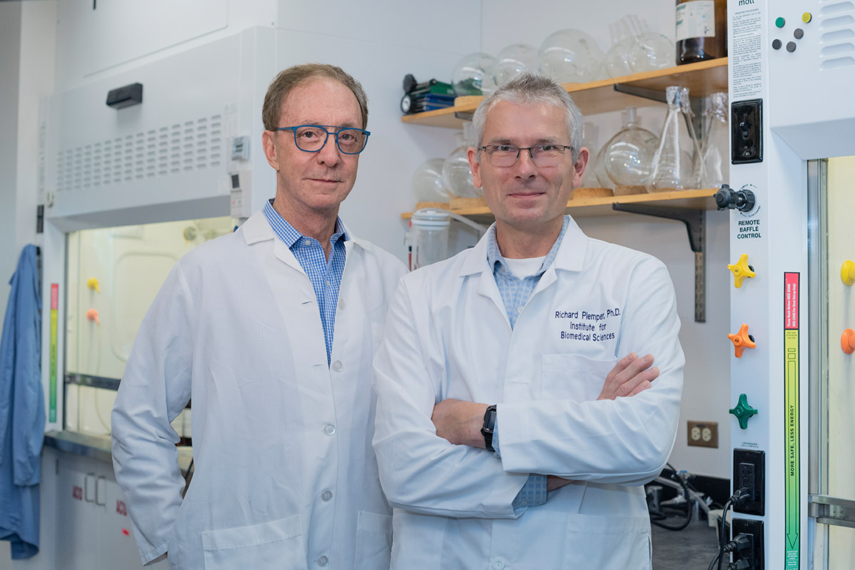 George Paiter and Richard Plemper pose in lab coats in a research lab.