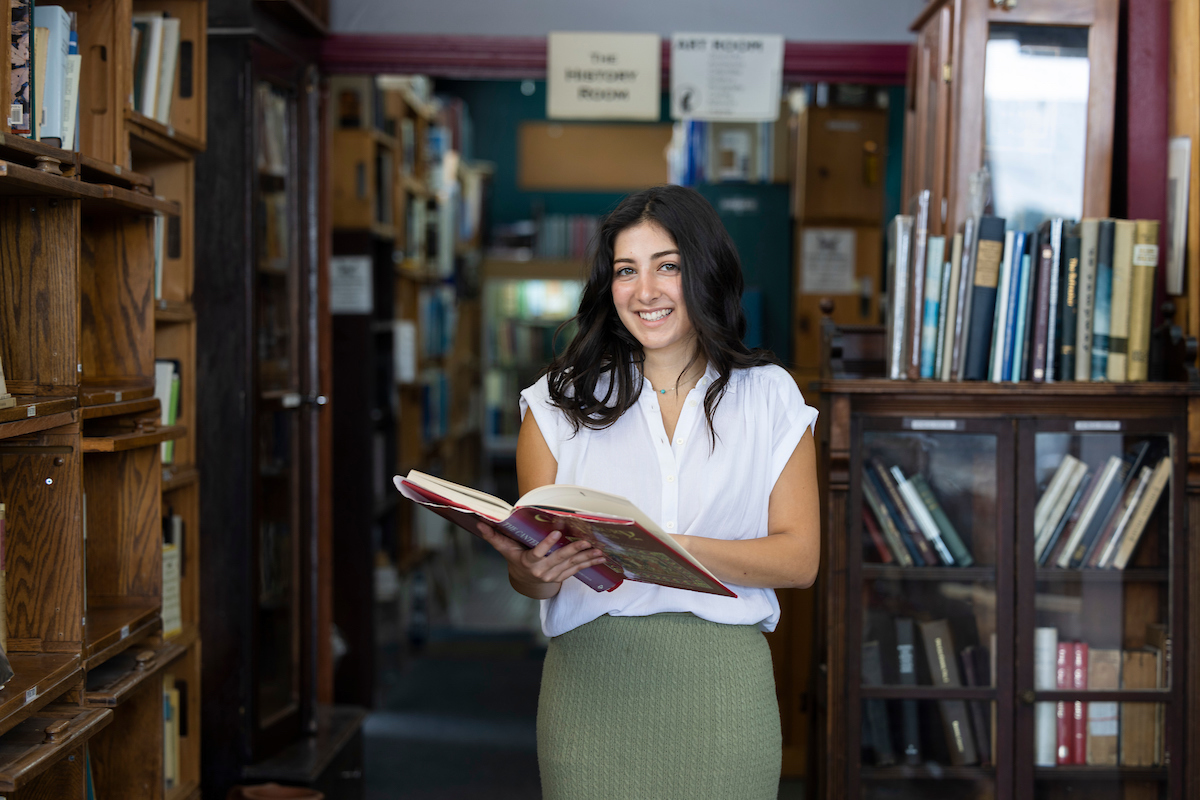 Alexa, standing with book in hand between two bookshelves