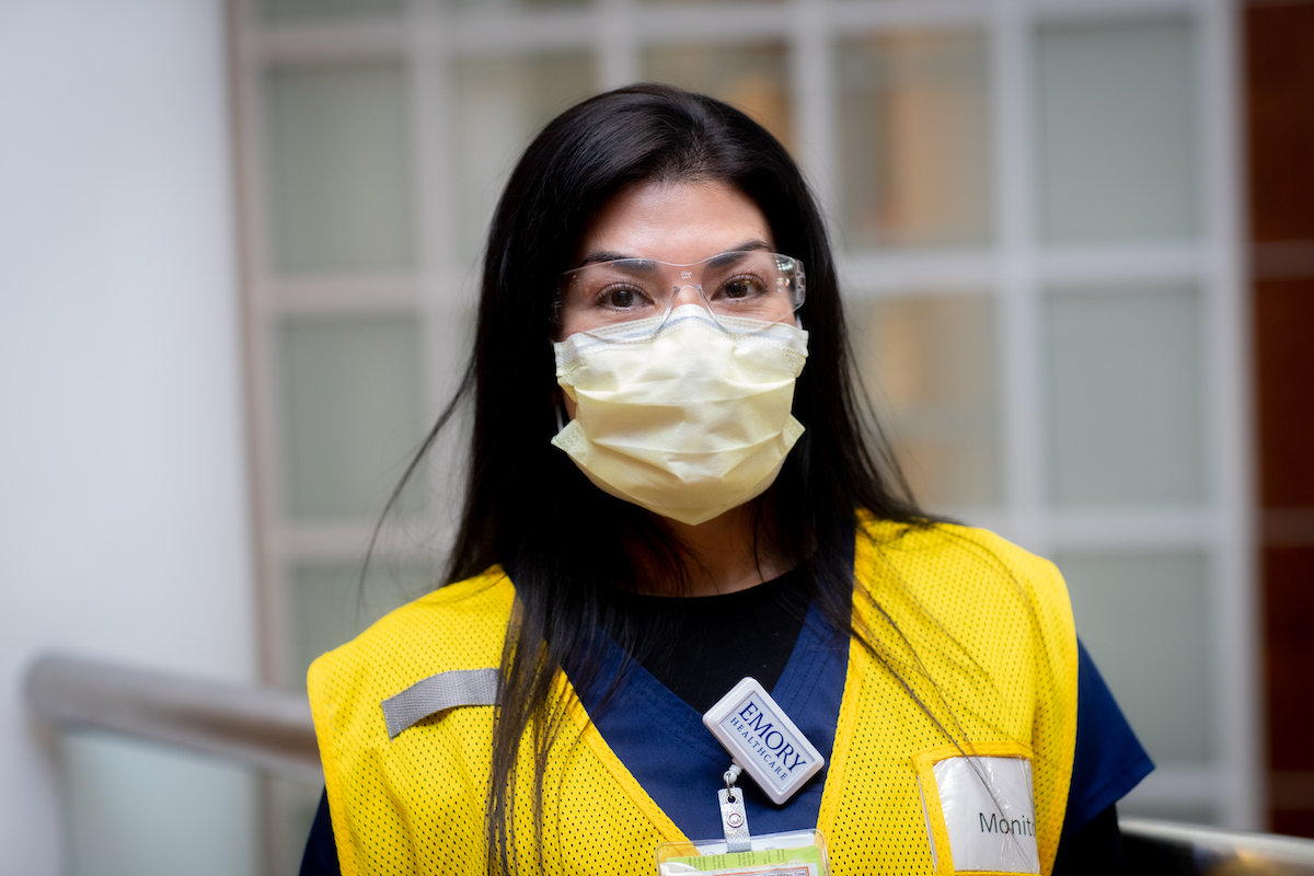Woman wearing Emory ID tag, yellow vest, and surgical mask.