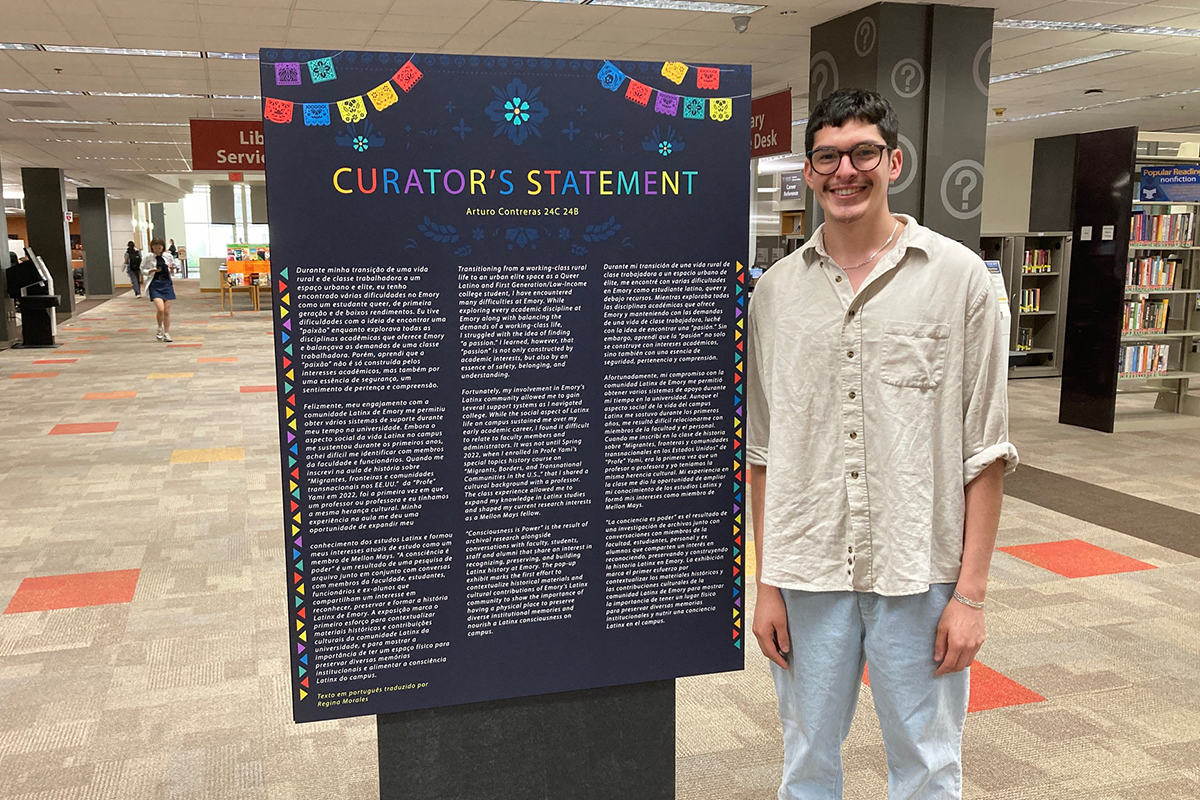 Photo of Arturo Contreras in library lobby standing beside poster-size Curator's Statement.