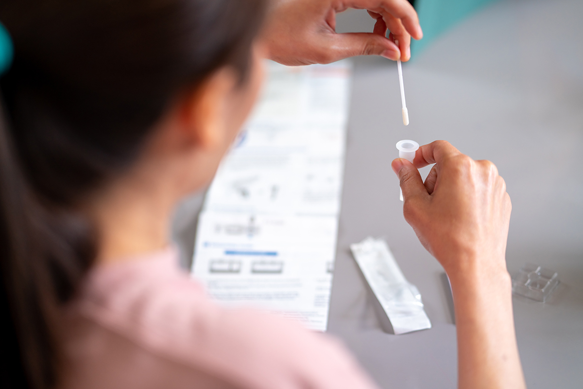 Photo: Over-the-shoulder shot of person inserting Q-tip into vial as done with COVID-19 tests