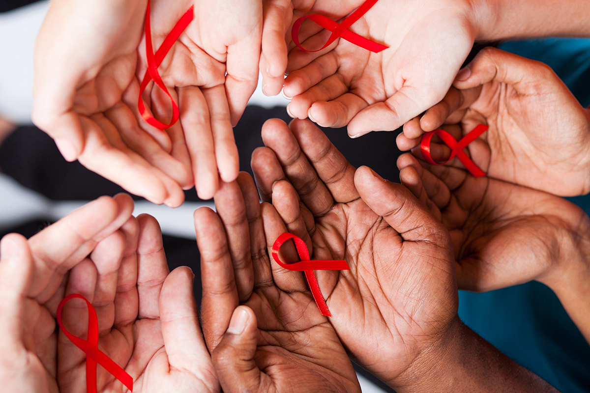 Photo: Several pairs of hands palms up holding HIV/AIDS awareness pin-on red ribbons