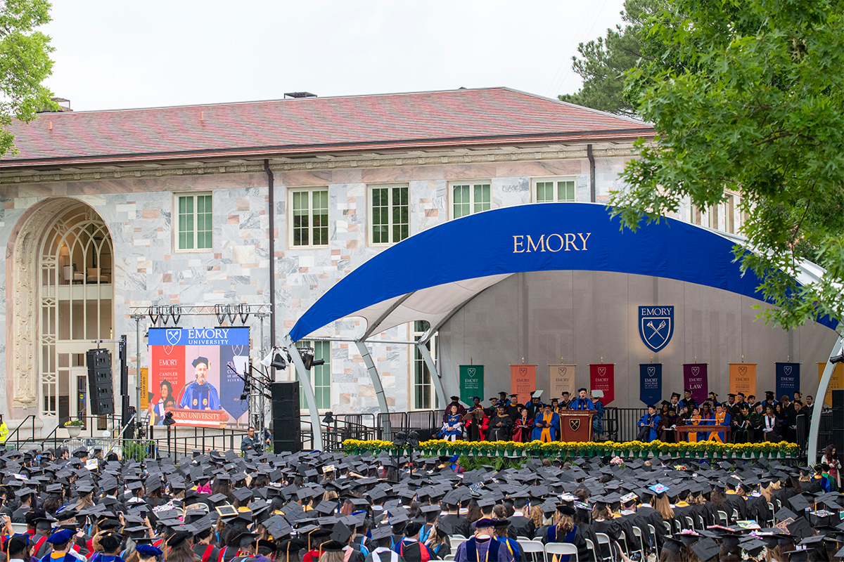 Photo of a sea of students in caps and gowns before Commencement stage, Convocation Hall in background