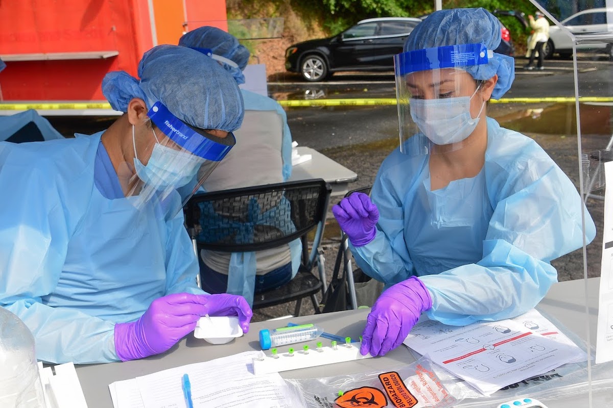 Photo of two masked health care workers conducting COVID-19 test at field location