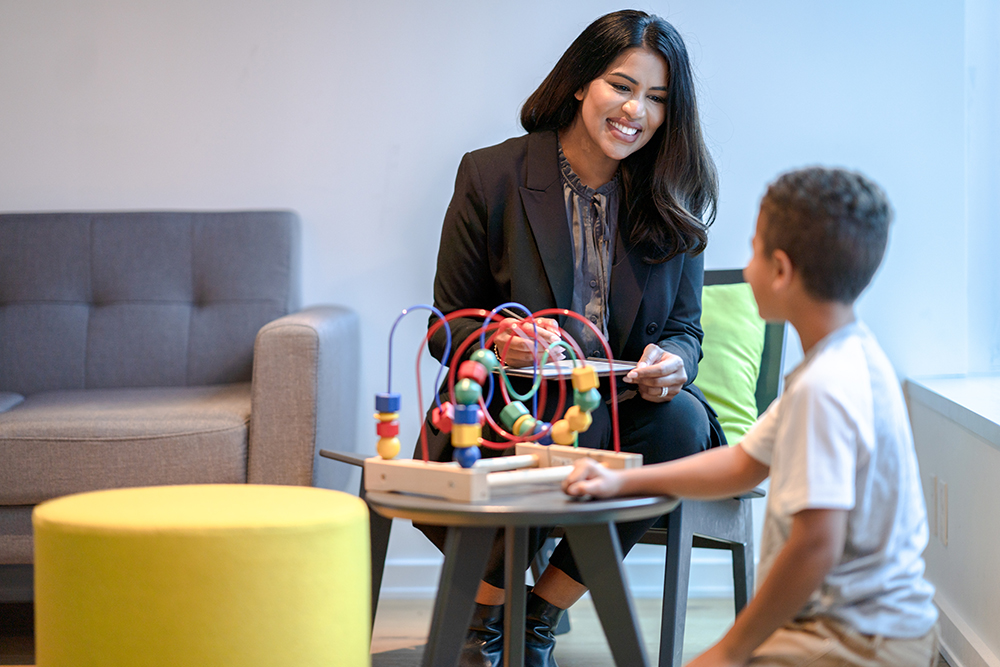 Photo: Woman in business attire talking with a child, a toy on a small table between them