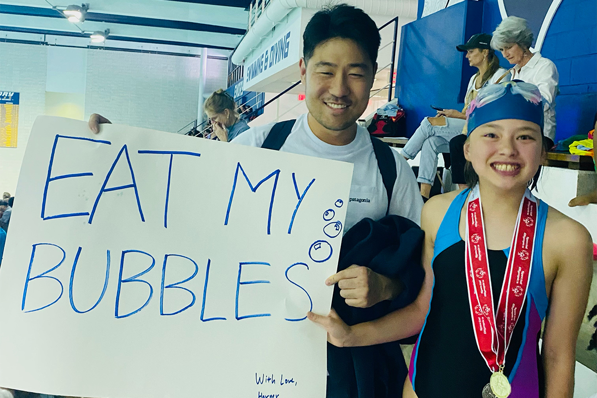 Photo of a smiling young Special Olympics swimmer and Emory alum holding homemade sign: ''Eat my bubbles''