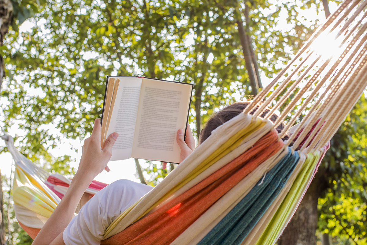stock photo of a person lying in a multicolored hammock, reading