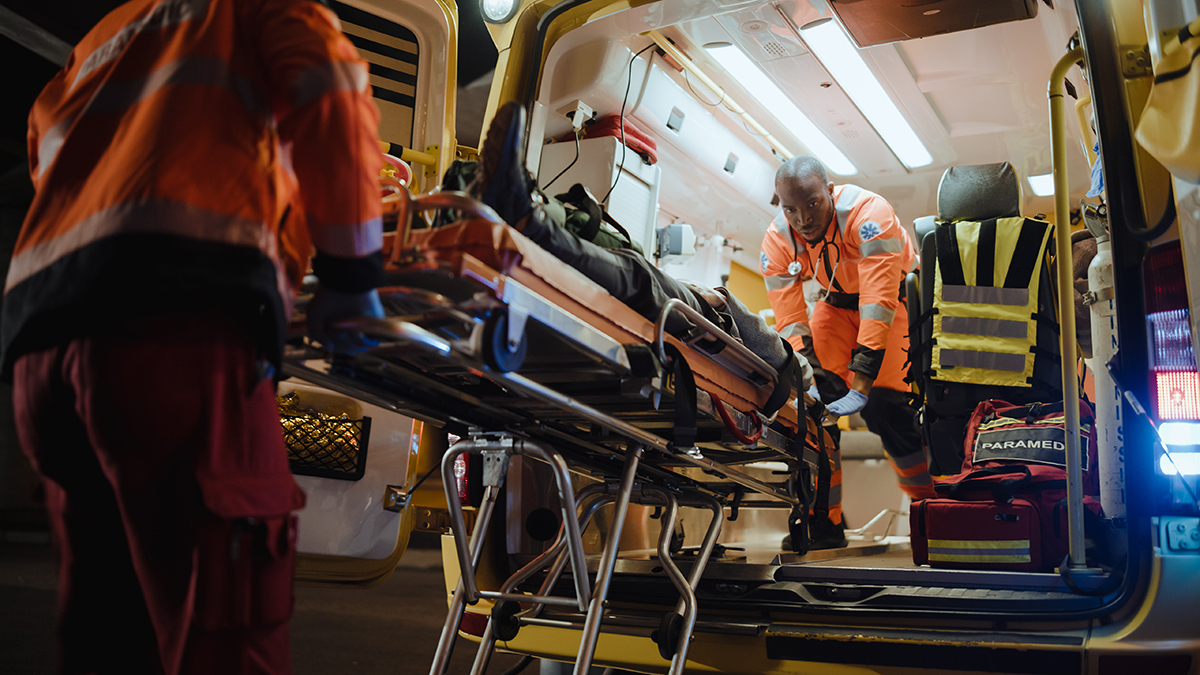 Patient is loaded into ambulance on a stretcher by EMTs.