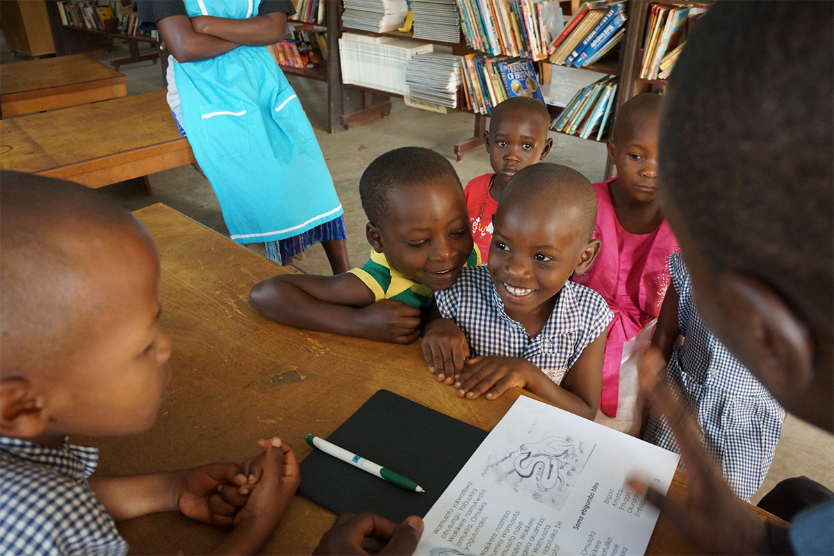 children in Uganda around a table reading a book
