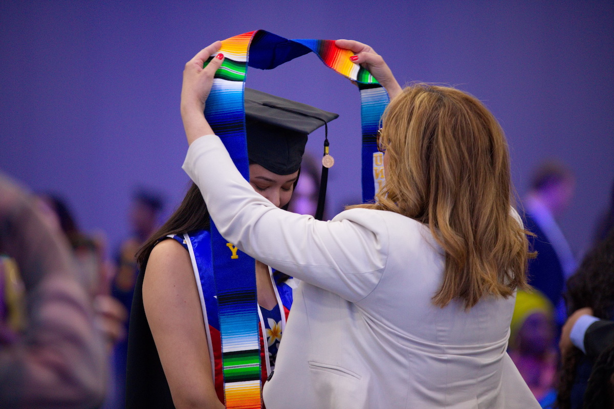 a person placing a stole over a graduate's neck