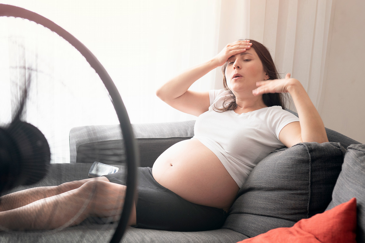 Pregnant woman on a hot day next to a fan