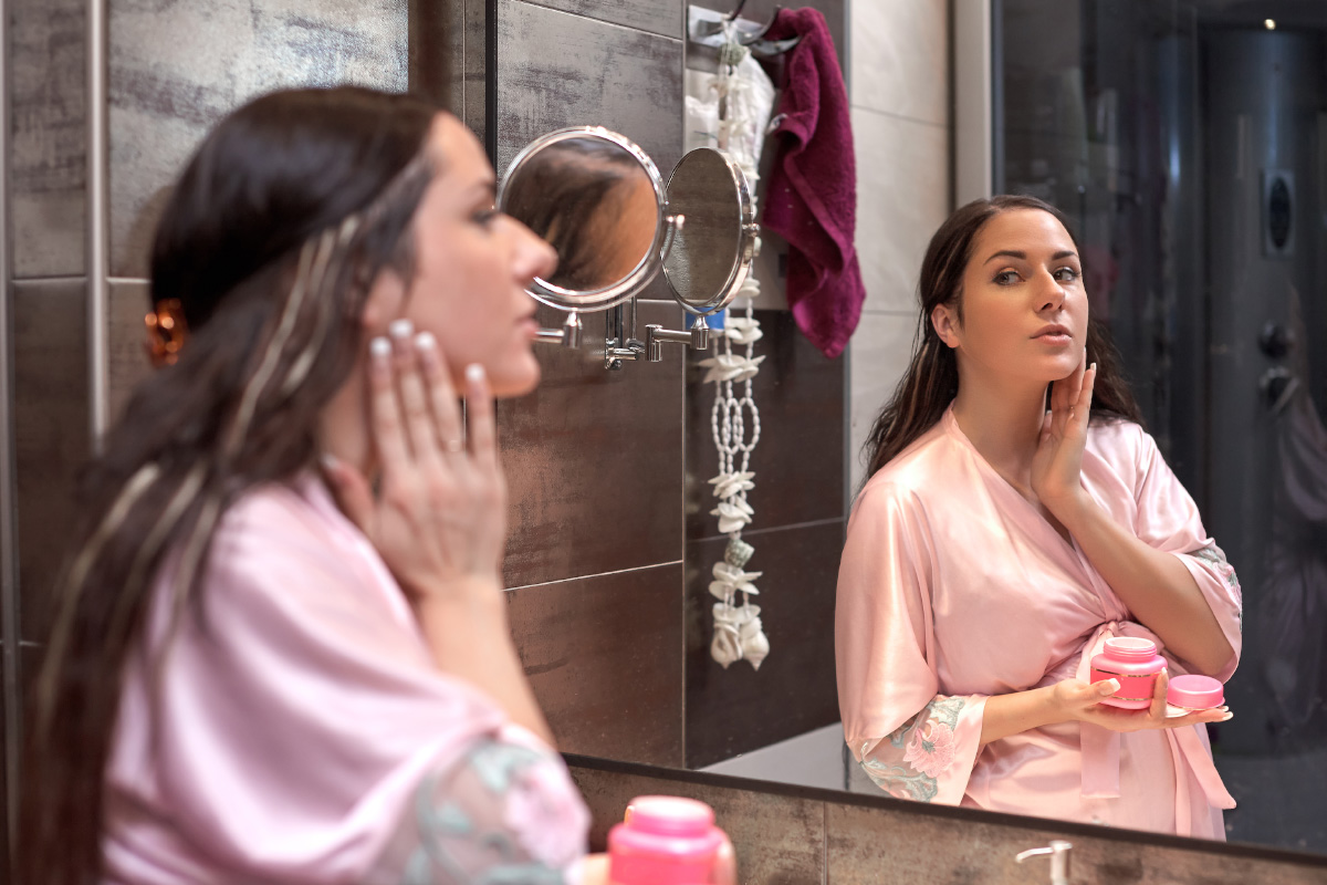 Young pregnant woman applying lotion to her facte