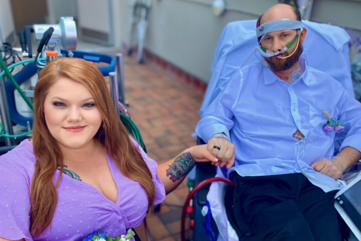 Woman in purple dress holds Man in button up Hooked up to ECMO machine 