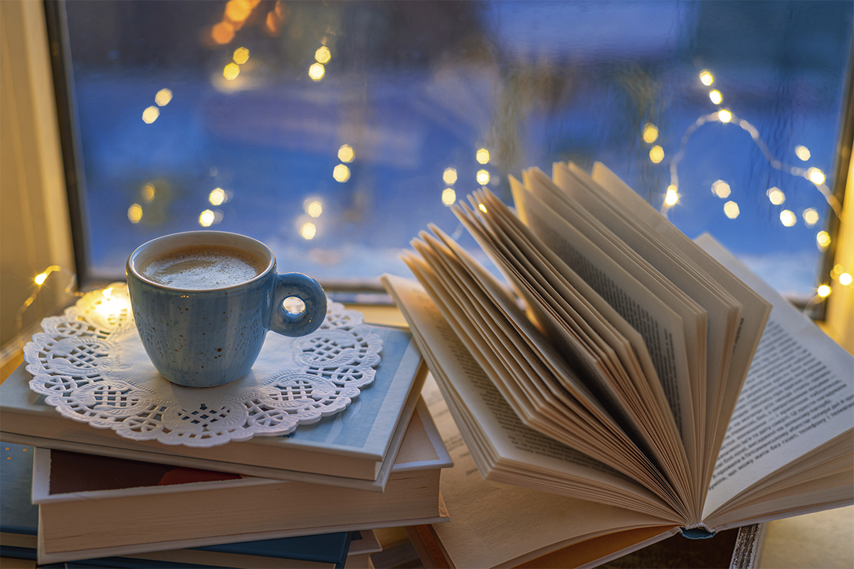 cup of cocoa beside open book in front of window