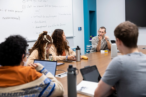 Faculty speaking to students seated around a table in a classroom