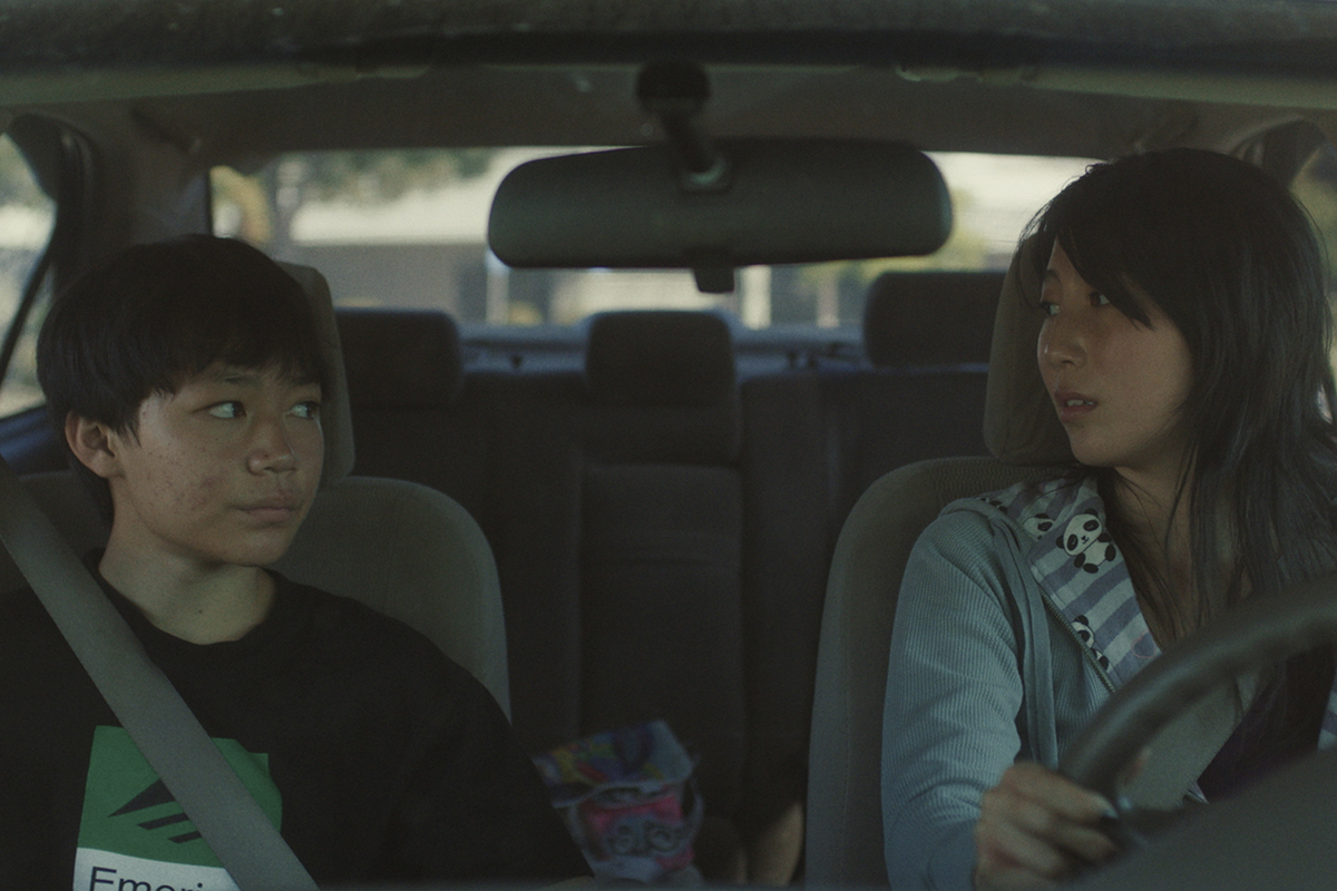 young boy and older girl sit in front seat of car looking at each other