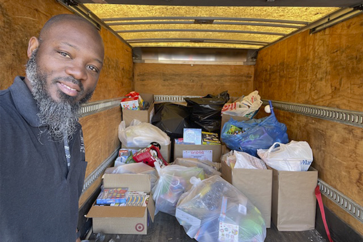 man standing outside of box truck with bags full of toys inside