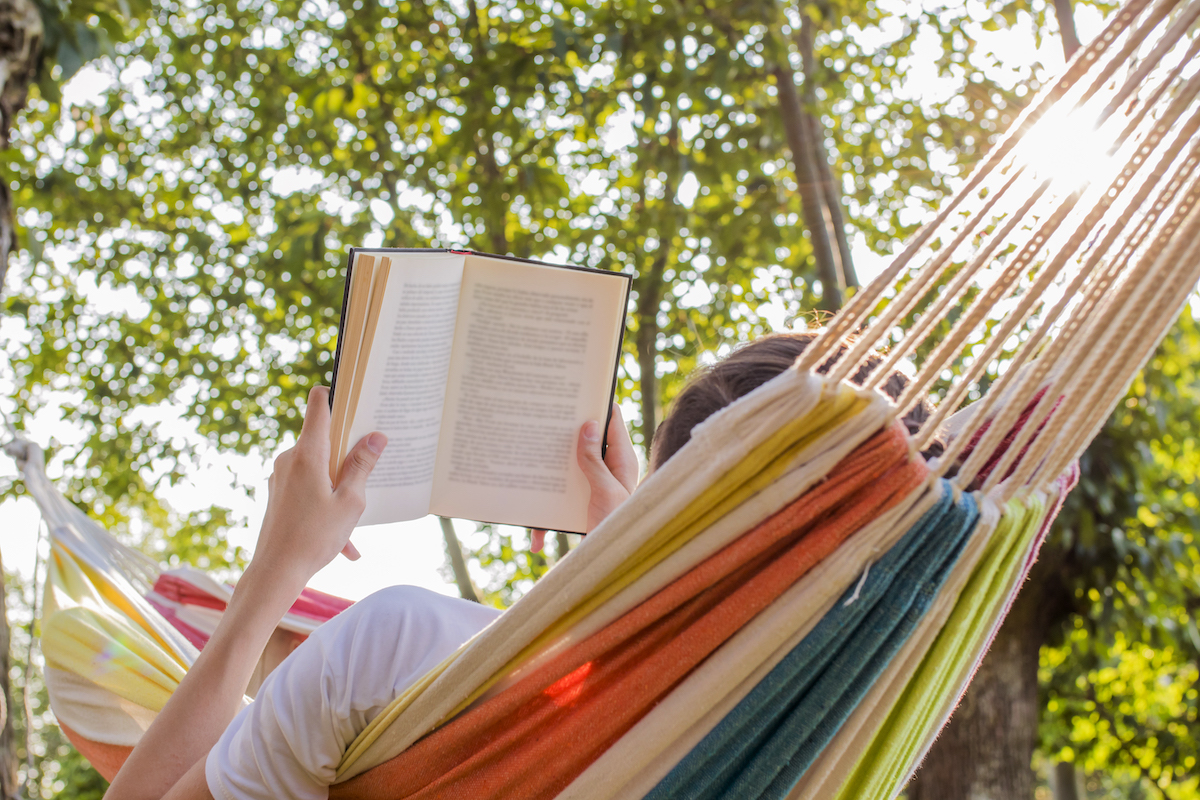 person laying in a hammock reading a book