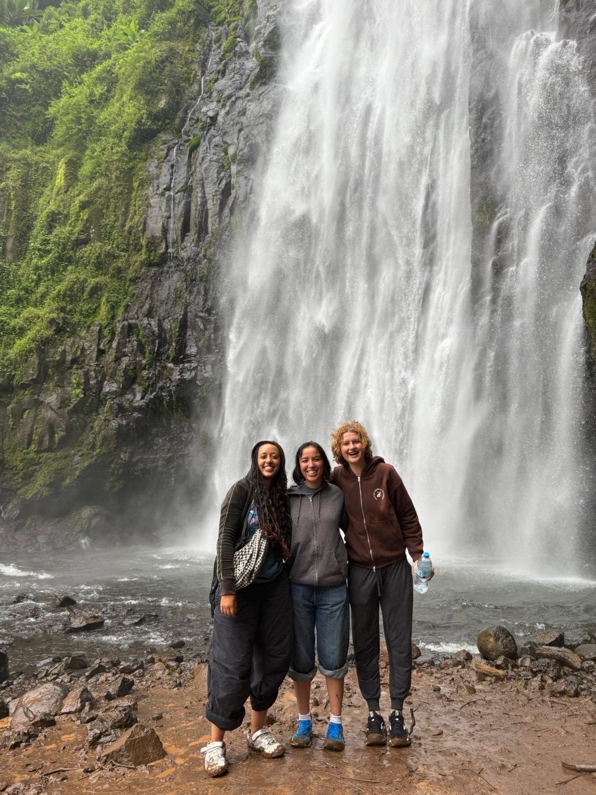 Three young women standing in front of a waterfall