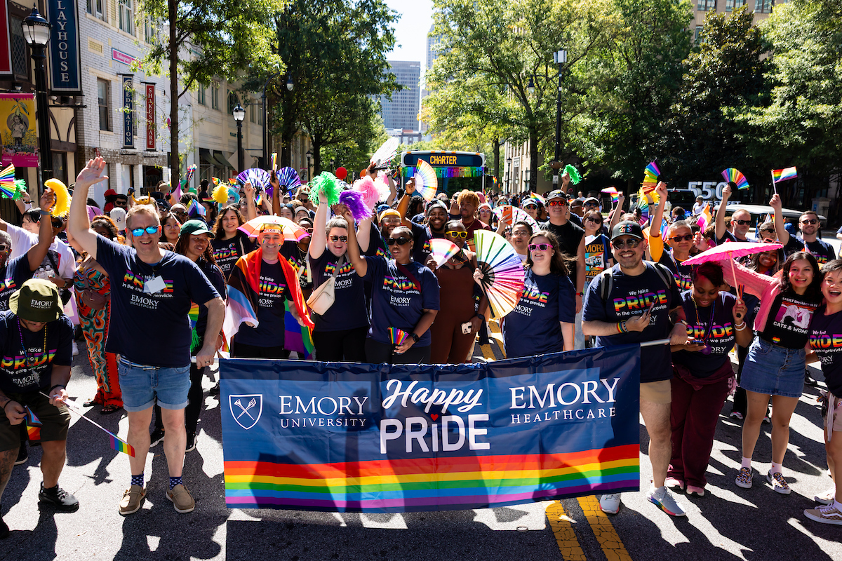 Large group walking behind Emory Pride banner