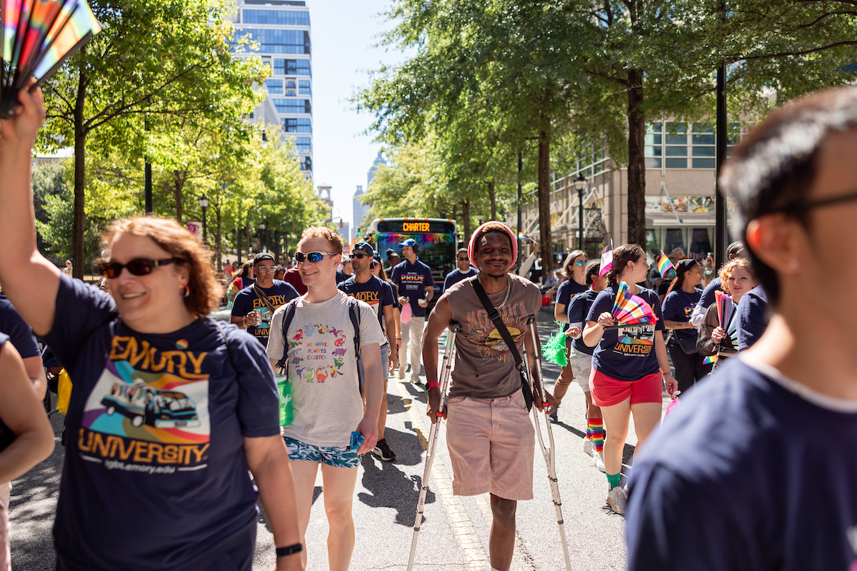 Parade goers, centered on a man walking the route with crutches and an amputated limb