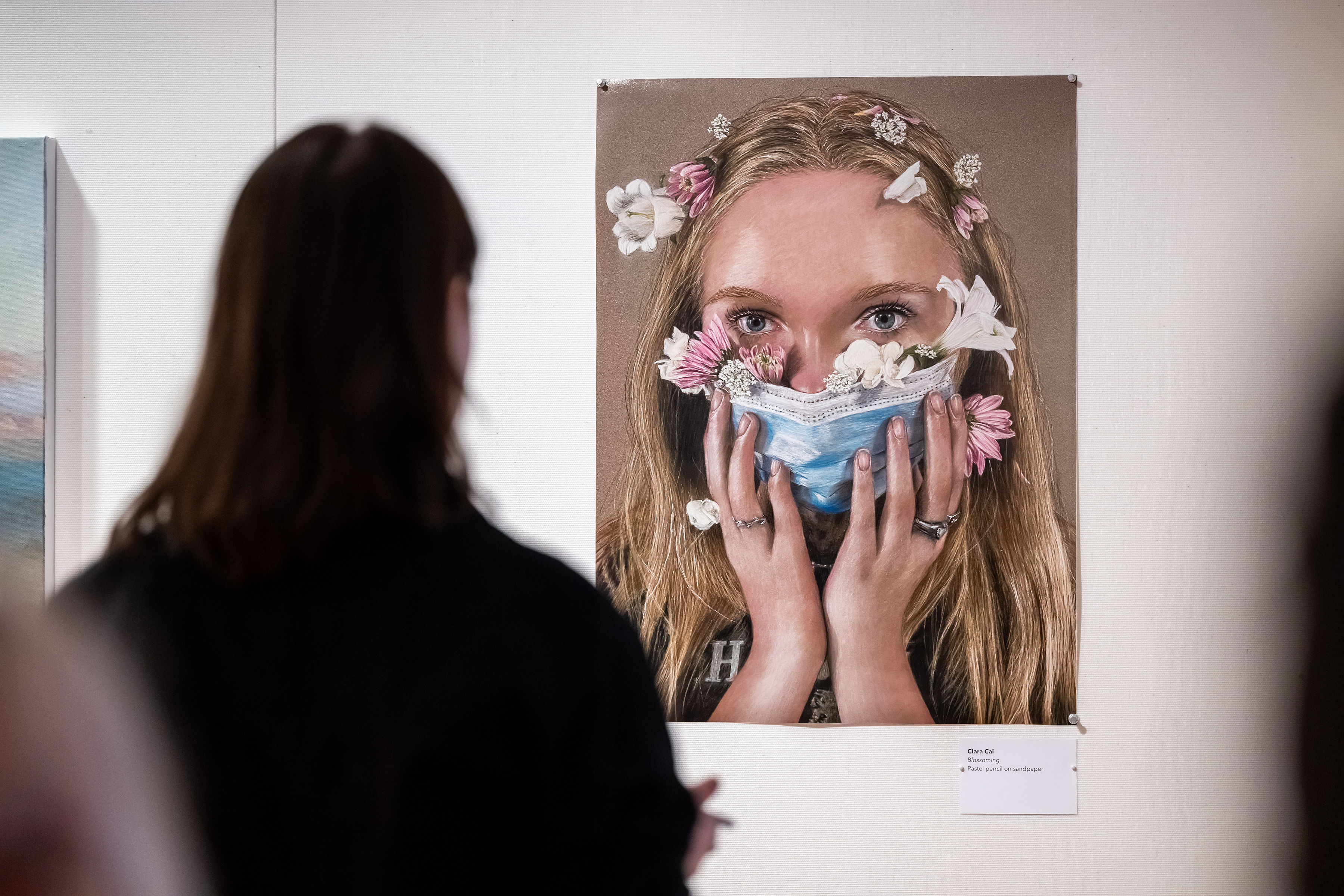 Woman looking at a portrait of a woman with flowers growing out of her surgical mask
