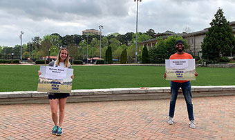 Two staff members hold up signs welcoming students to campus