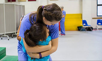 An Emory student wearing scrubs hugs a child as she volunteers