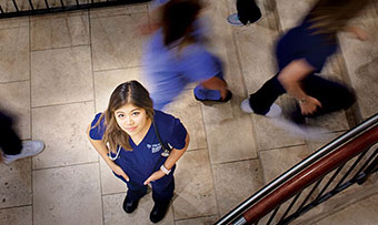 An Emory nursing student poses in her scrubs at the bottom of a staircase