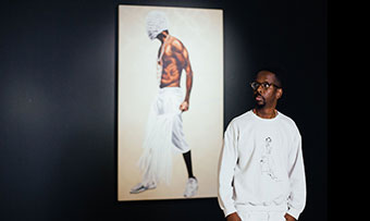 Fahamu Pecou stands in front of a wall displaying his art
