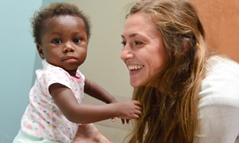 A medical student smiles while caring for Sara, a Haitian baby with a rare birth defect
