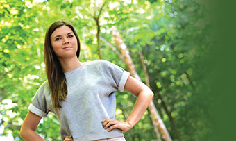 A photo of recent college graduate Kendall Lasseter, who was diagnosed with Lyme disease, in front of a wooded area.