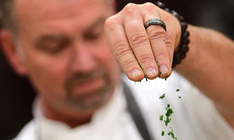 A chef sprinkles a green herb on a dish